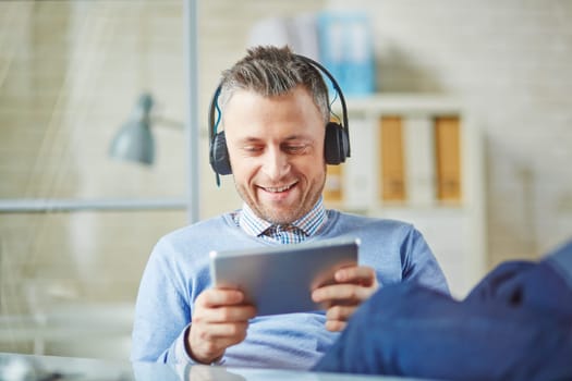 Happy businessman with earphones using touchpad