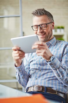 Smiling businessman in eyeglasses reading information in touchpad
