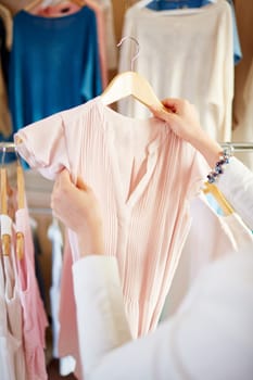 Young female holding pink chiffon blouse on hanger