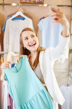 Beautiful young woman with new dress making selfie in department store