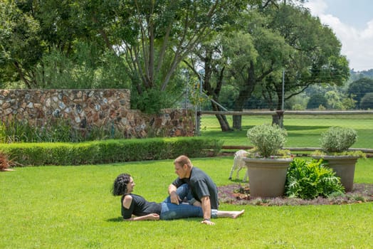A couple sit on the lawn in their garden enjoying the nice summer weather, while chatting to each other.