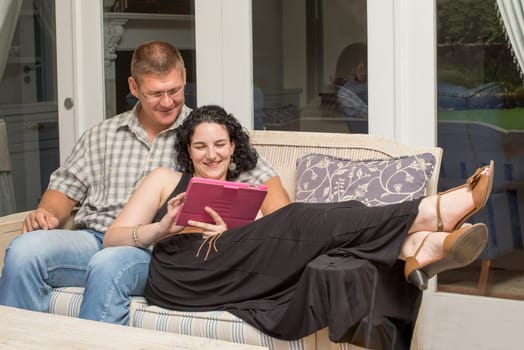 A young couple sitting on the bench on the patio, while viewing something on a tablet.