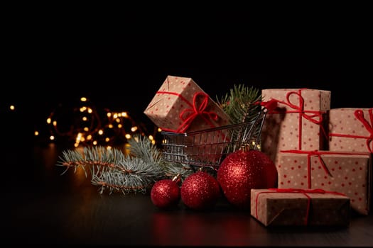 Shopping trolley, gift boxes and Christmas decoration with LED lights garland on a black background with copy space, Christmas and New Year shopping. Winter sale.