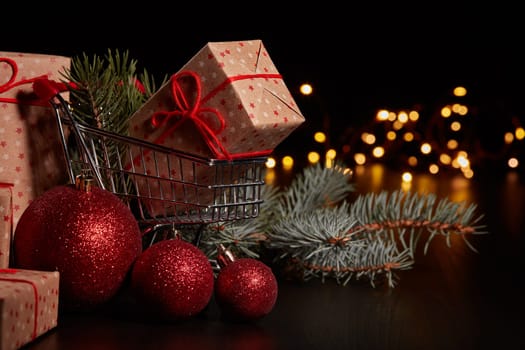 Shopping trolley, gift boxes and Christmas decoration with LED lights garland on a black background, Christmas and New Year shopping. Winter sale.