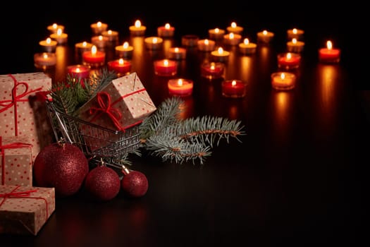 Shopping trolley, gift boxes and Christmas decoration with burning candles on a black background with copy space, Christmas and New Year shopping. Winter sale.