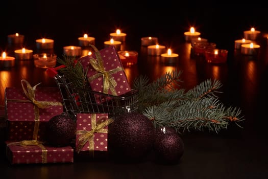 Shopping trolley, gift boxes and Christmas decoration with burning candles on a black background, Christmas and New Year shopping. Winter sale.
