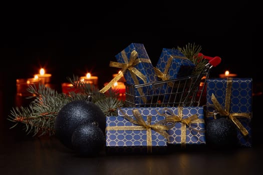 Shopping trolley, gift boxes and Christmas decoration with burning candles on a black background, Christmas and New Year shopping. Winter sale.
