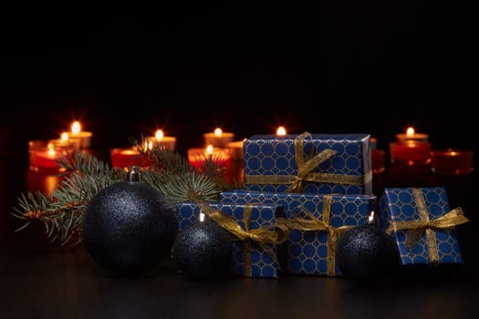 Gift boxes, Christmas decoration with burning candles and fir tree branch on black background with copy space. Christmas and New Year shopping. Greeting card