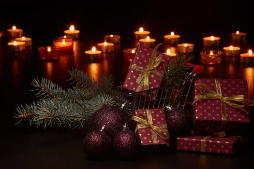 Shopping trolley, gift boxes and Christmas decoration with burning candles on a black background, Christmas and New Year shopping. Winter sale.