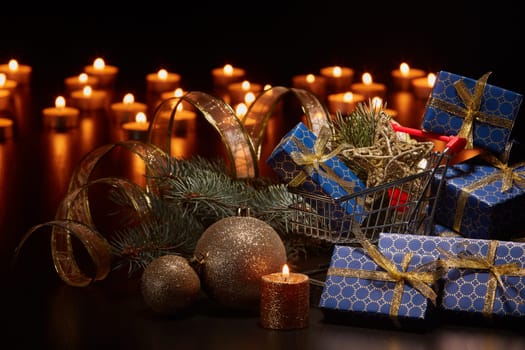 Shopping trolley, gift boxes and Christmas decoration with burning candles and fir tree branch on black background, Christmas and New Year shopping. Winter sale.