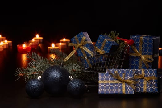 Shopping trolley, gift boxes and Christmas decoration with burning candles on a black background, Christmas and New Year shopping. Winter sale.
