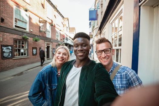 A selfie shot of two men and one woman on a city street. They are smiling at the camera.
