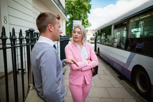 Two businesspeople waiting for a bus on a city street.