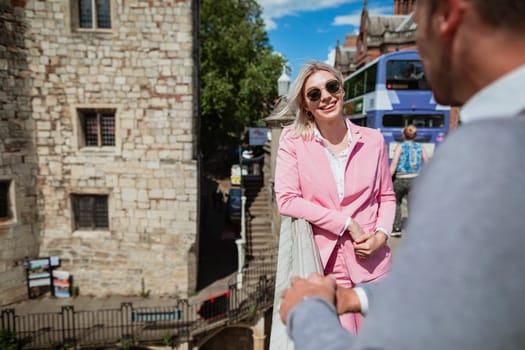 Two businesspeople standing and talking on a bridge. The main focus is on a woman smiling at the man she is talking to.