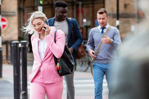 Businesspeople walking home after a day of work. The main focus is on one businesswoman walking in front of people while talking on her mobile phone.