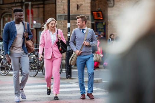 A businesswoman walking with two businessmen home from work through the city. They are walking over a zebra crossing.