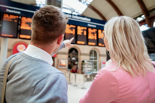 A businessman and businesswoman looking at a departure board in a train station.