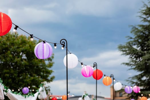 A wide shot of paper lanterns hanging up alongside a set of string lights at a garden party.