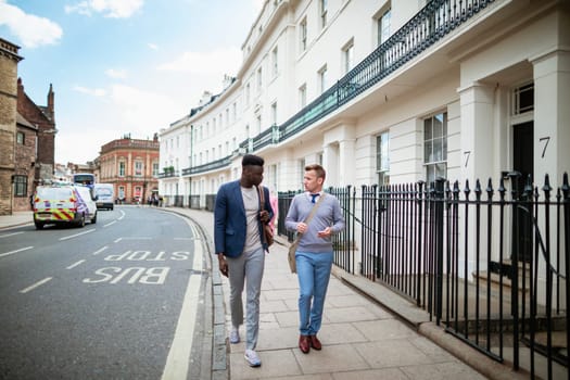 Two businessmen walking, on their way to work. They are talking and one man is holding a mobile phone ready to use it.