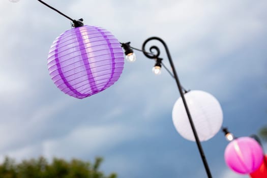A close-up of paper lanterns hanging up alongside a set of string lights at a garden party.