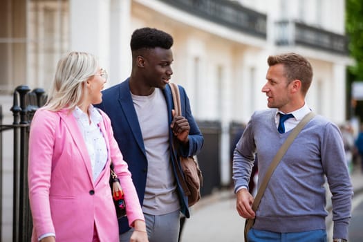 Two businessmen and one businesswoman walking to work while having a discussion.