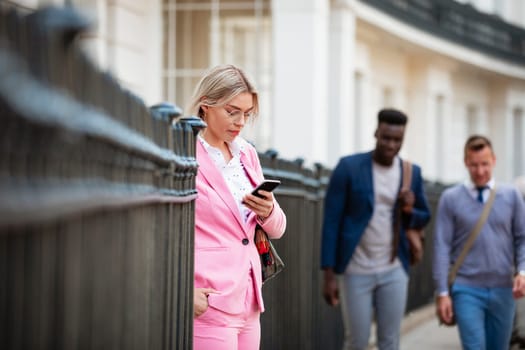 Businesswoman standing on a city street whilse using her phone. Two businessmen are about to walk past.