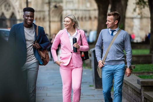 A businesswoman is walking with two businessmen to work through the city.