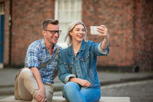 A woman taking a selfie with a man while sitting down on a bench.