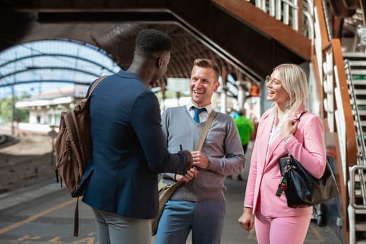 Two businessmen and one businesswoman standing in a train station having a discussion. They are laughing together.