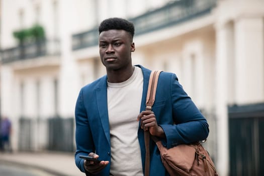 Businessman walking down a street on his way to work with a bag strap over his shoulder. He is holding his phone in one hand as if ready to browse the Internet but he is looking ahead.