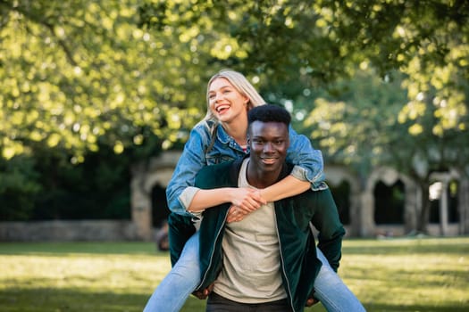 A man giving a woman a piggyback lift through a park. They are both smiling.