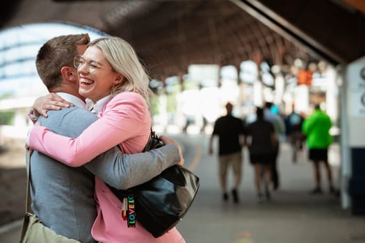 A male and female co-worker parting ways after work. They are hugging each other goodbye while laughing.