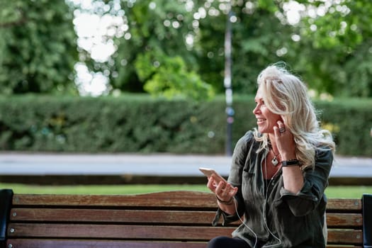 A woman sitting on a park bench listening to music on her MP3 player while looking sideways.