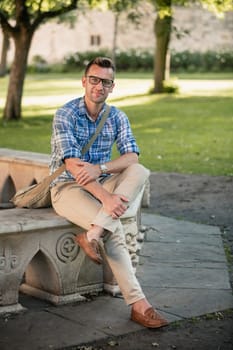A man wearing casual clothing, sitting on a stone bench in the park.