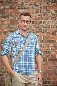 A man standing in front of a brick wall and looking into the camera while smiling.