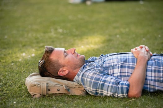 A close-up of a man laying his head on his bag in the park.