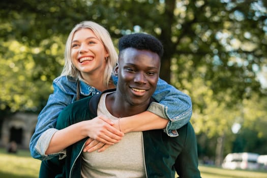 A close-up shot of a man giving a woman a piggyback lift through a park. They are both smiling.