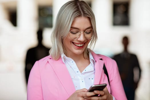 A businesswoman looking down at her phone and typing while smiling.
