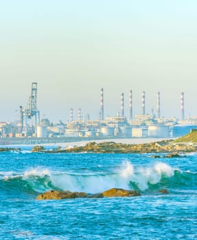 Industrial plant pipes by the seashore, port equipment, freight cranes, waves brеaking on shore in sunlight, Porto, Portugal
