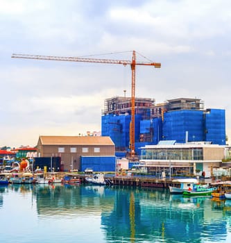 Construction site by Limassol waterfront, boats moored in marina with cafes and restaurants, Cyprus