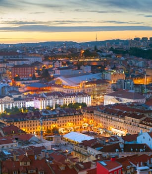 Aerial night cityscape of Lisbon downtown, red rooftops, illuminated Praca do Pedro IV square, afterglow skyline, Portugal