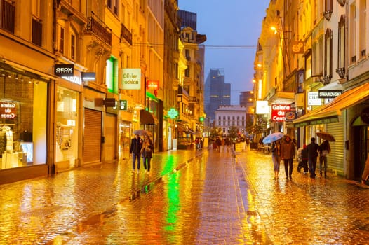BRUSSELS, BELGIUM - OCTOBER 06, 2019: People walking by Old Town shopping street of Brussels in the rain at twilight