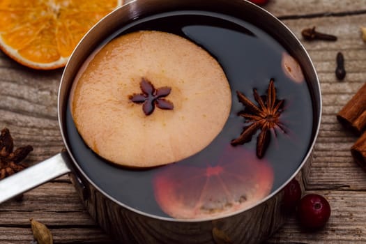 Small stewpot with mulled wine and cinnamon sticks, slice of oranges and apple on wooden table top view. Hot winter drink. Christmas beverage.