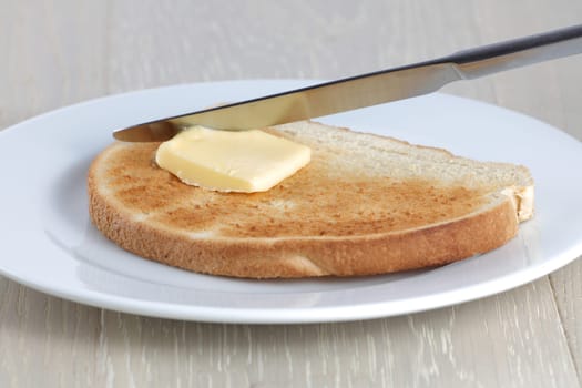 A slice of toast knife and butter on a white plate