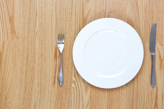 A dining fork and knife beside a plate on a wood table with copy space