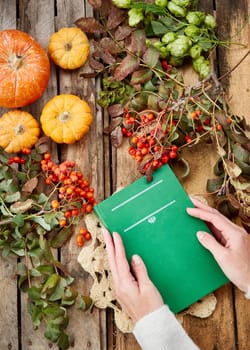Autumn time. Book in hand, pumpkins and yellow leaves on a wooden background. Fall season. Autumn mood
