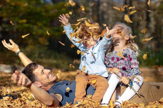 Happy dad and children playing with autumn leaves in forest