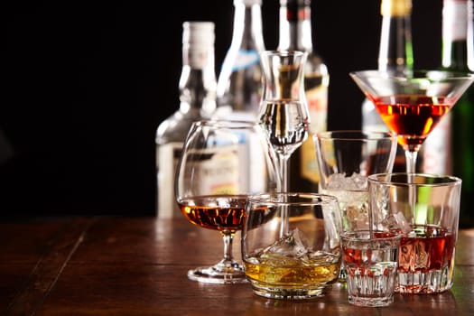 Large assortment of different cocktails in glasses on a bar counter at night with copy space