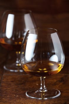 Two filled cognac snifter glasses viewed in close-up on dar brown wooden counter surface in selective focus