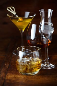 Whisky on the rocks, martini, cognac and liqueur in elegant glasses on a rustic wooden bar counter in shadowy light conceptual of partying and nightlife